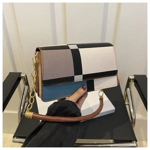 Detail of color-block flap handbag with gold chain strap held by model in minimalist setting