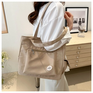 Detail of beige nylon tote bag with zippered outer pocket and 'good luck' circular patch
