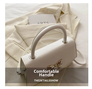 Detail shot of white leather square handbag with silver bow accent on beige blazer