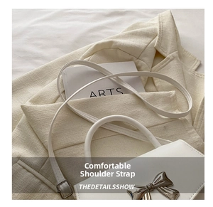 Detail of white leather crossbody bag with silver bow ornament and slim shoulder strap