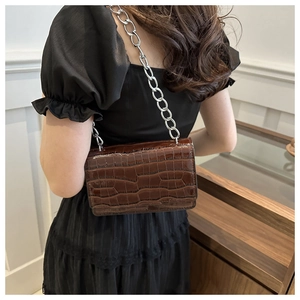 Detail of dark brown croc-embossed flap bag with stylish silver metal chain strap