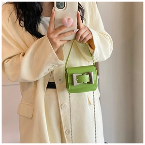 Detail of green mini crossbody bag with large silver buckle and chain strap on cream blazer