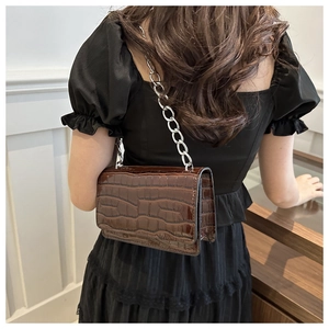 Detail of dark brown faux crocodile crossbody bag with silver chain strap on model