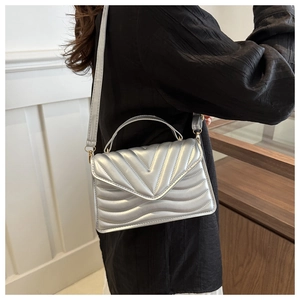 Detail view of silver quilted crossbody bag with V-shaped stitching and top handle strap