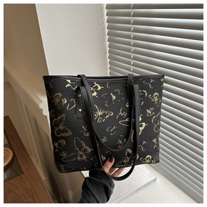 Detail of black tote bag featuring gold butterfly embroidery and textured PU leather