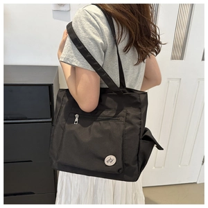 Detail of a black large-capacity tote bag with a circular 'good luck!' badge and side pockets