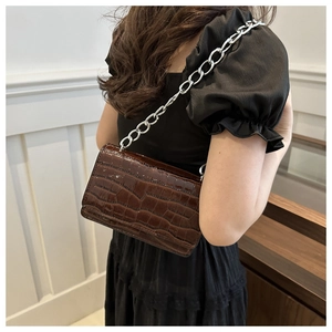 Detail of dark brown faux-croc crossbody bag featuring a chunky silver chain strap