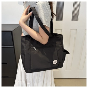 Detail view of black nylon tote bag featuring front zipper pocket and good luck slogan