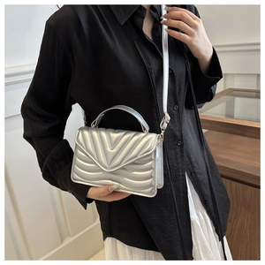 Detail of silver crossbody bag with V-quilted pattern and leather shoulder strap