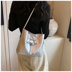 Silver shoulder tote bag with decorative cross-lacing and metallic bow detail worn by model