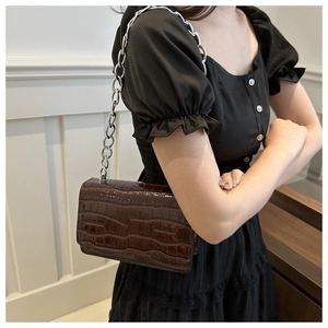 Detail of dark brown faux-croc leather crossbody bag with silver metal chain strap
