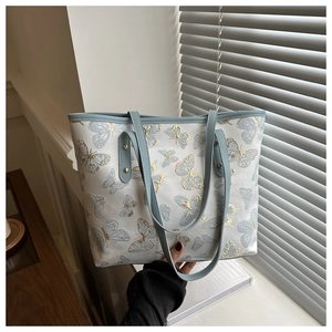 Detail of blue butterfly embroidery on white canvas tote bag with leather strap