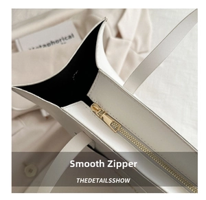 Detail of smooth gold zipper on a white leather tote bag with elegant black lining