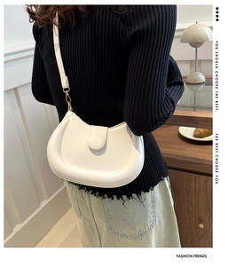 Detail of a minimalist cream-white saddle bag featuring a matching oversized buckle