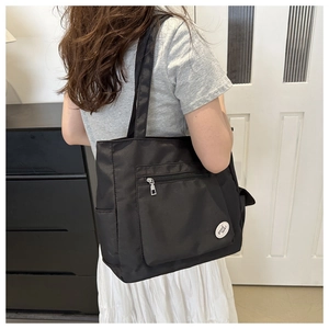 Detail of waterproof black nylon tote bag with front zipper pocket and decorative logo