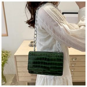 Detail of dark green crocodile texture on glossy crossbody bag with silver chain