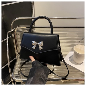 Detail of a black trapezoid bag with silver bow hardware on a modern display stand