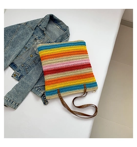 Flat lay of colorful striped straw tote bag with brown leather handles on denim jacket