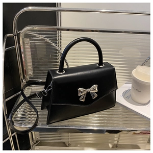 Detail of a black crossbody bag with a polished silver metal bow and detachable strap