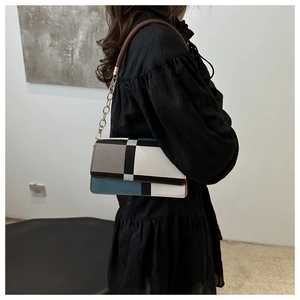 Detail of color-block shoulder bag featuring blue, grey patches and gold chain strap