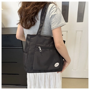 Detail of black nylon tote bag with a zipper pocket and a white good luck patch