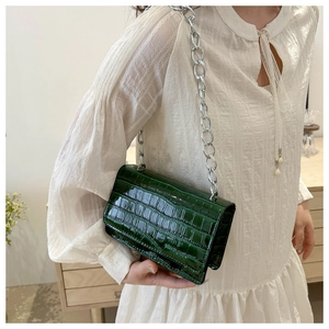Detail of dark green crocodile texture crossbody bag with silver chain on model