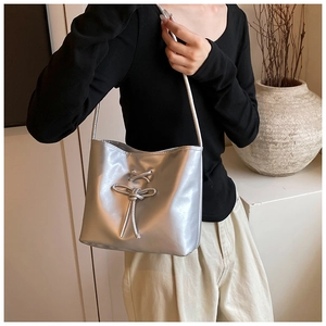 Detail of silver metallic bucket bag with knot detail worn by a model in a minimal setting