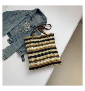 Detail of handwoven straw tote bag featuring striped texture and dark brown PU straps