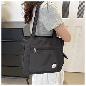 Detail of black canvas tote bag showing outer zipper pocket and Good Luck patch