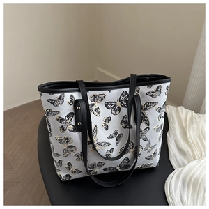Close-up of elegant butterfly embroidery and gold rivet details on a grey tote bag