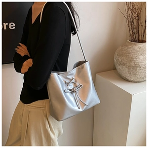 Sac seau argenté avec détail de nœud porté à l'épaule dans un décor minimaliste