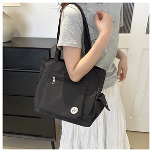 Detail of a black nylon tote bag featuring a front zipper pocket and a round graphic patch