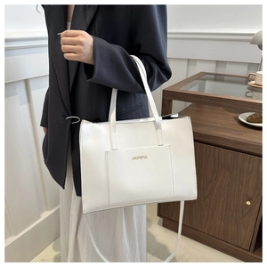 White minimalist tote bag with outer pocket and adjustable strap on elegant female model