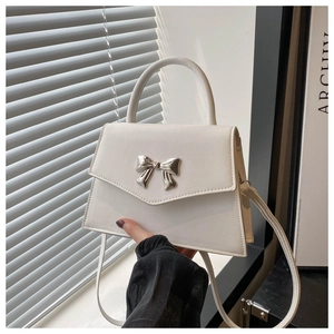 Close-up of white leather handbag featuring a stylish silver metallic bow buckle detail