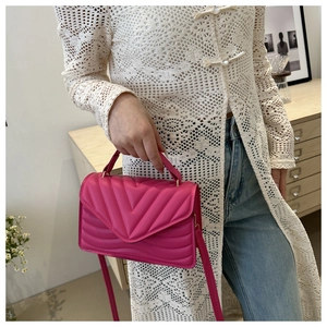 Detailed view of magenta crossbody bag with V-quilted pattern and top handle on a model