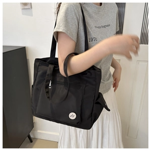 Close-up of black canvas tote bag with side pockets and a Good Luck badge detail