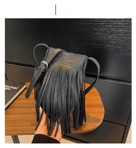 Detail of black pebbled leather fringe crossbody bag with silver buckle on a wooden table