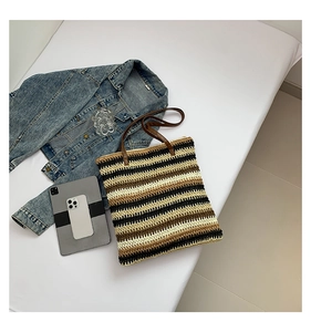 Flat lay of a large striped straw tote bag with brown straps and everyday lifestyle items