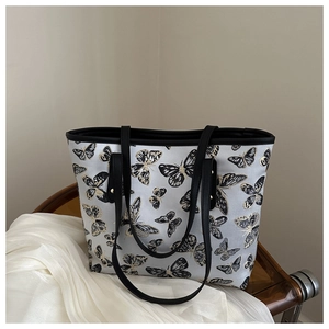 Detail of butterfly print tote bag showing black leather straps and rivet accents