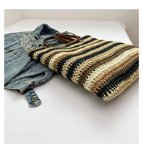 Detail of hand-woven striped tote bag with brown leather straps and textured straw finish
