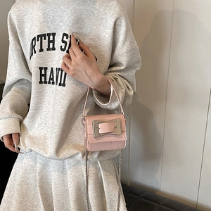 Pink leather mini crossbody bag with metal buckle and chain strap shown on a model