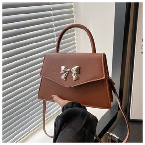 Detail of caramel leather handbag with silver metallic bow and top handle
