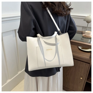 Detail of white faux leather tote bag with gold lettering and adjustable shoulder strap