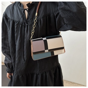 Detail of color-block geometric handbag with gold chain strap worn over a black dress