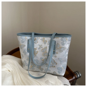 Detail of light blue tote bag featuring premium butterfly embroidery on a vintage chair