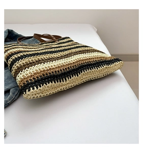 Detail of hand-woven straw tote bag with striped texture and durable leather handles