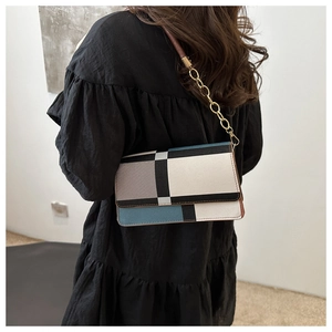 Close-up of geometric color-block shoulder bag with gold chain strap on black dress
