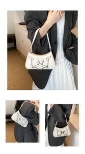 Detalle de bolso baguette blanco con mariposa de metal plateado y detalles de cadena