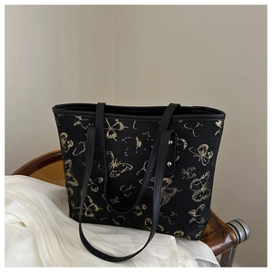 Detail of golden butterfly embroidery on black tote bag with metallic rivet accents