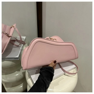 Detail of pink faux leather shoulder bag with sleek curved design and gold hardware